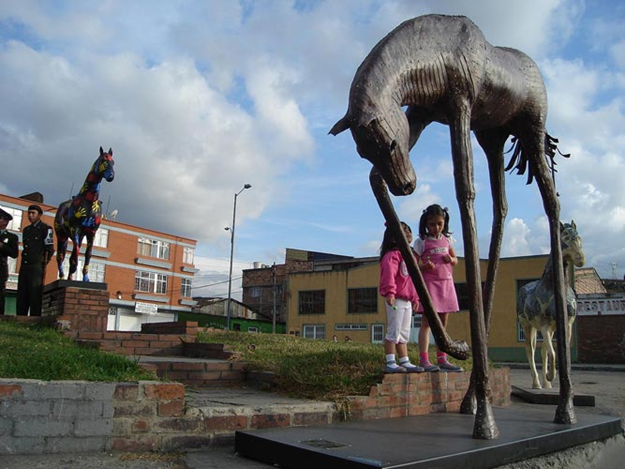 Iron horse sculpture titled "Miserere" by Joaquín Restrepo, placed in an outdoor setting, showcasing dynamic equine movement.